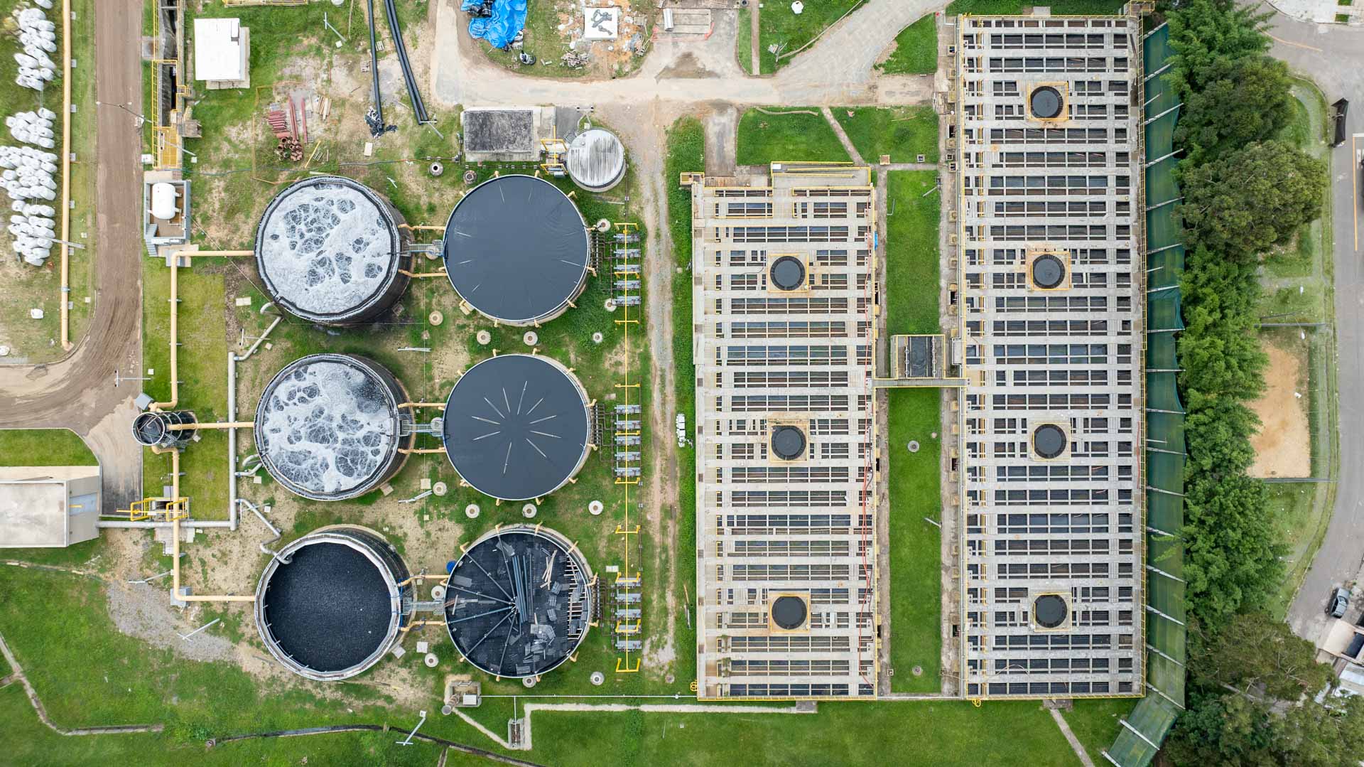 Vista aérea da Estação de Tratamento de Esgoto, mostrando seis tanques circulares e grandes reservatórios retangulares ladeados por área verde.