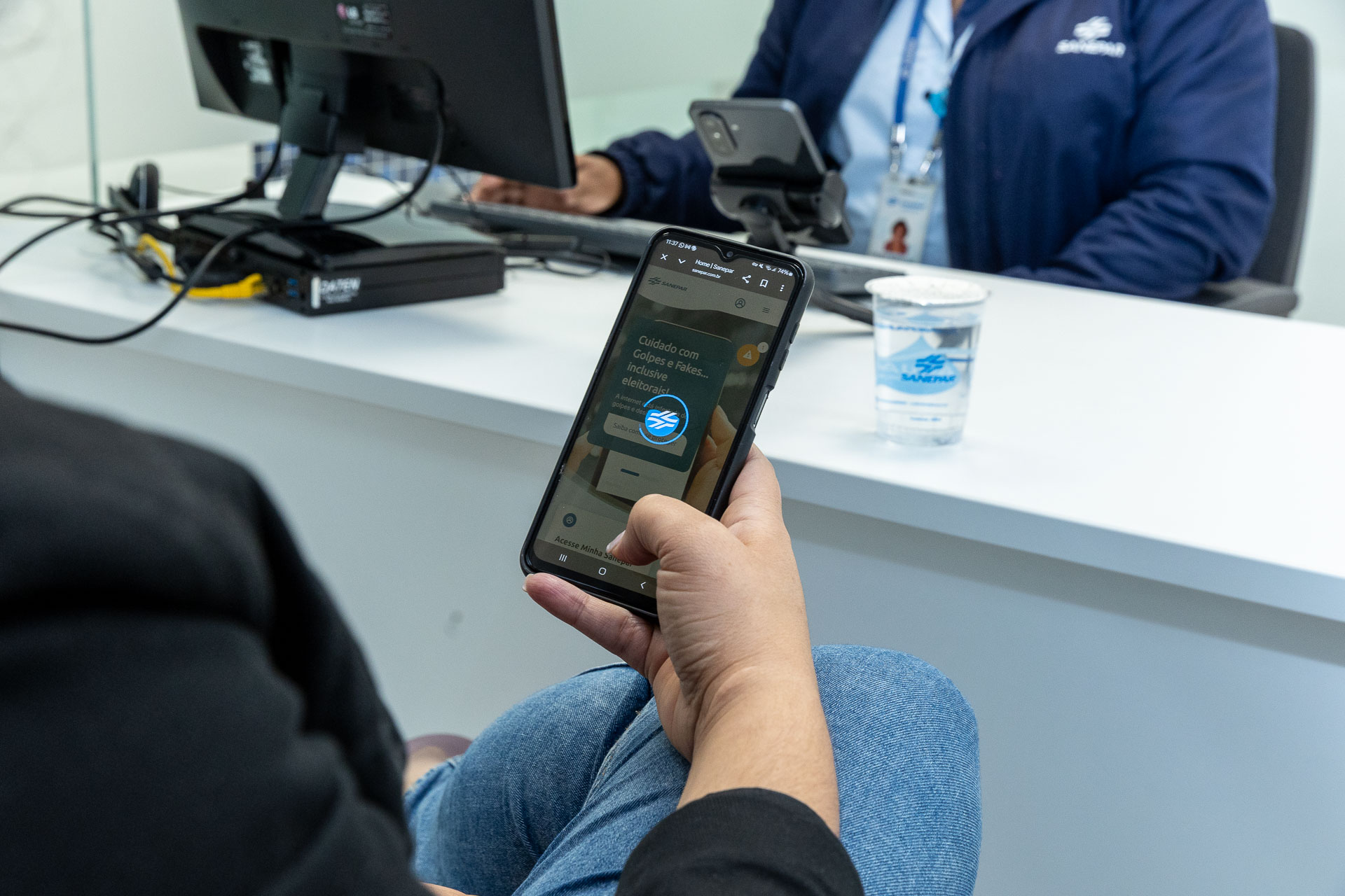 clientes está no atendimento da sanepar e está usando o celular. cliente tem cabelos cacheados e aparece de costas