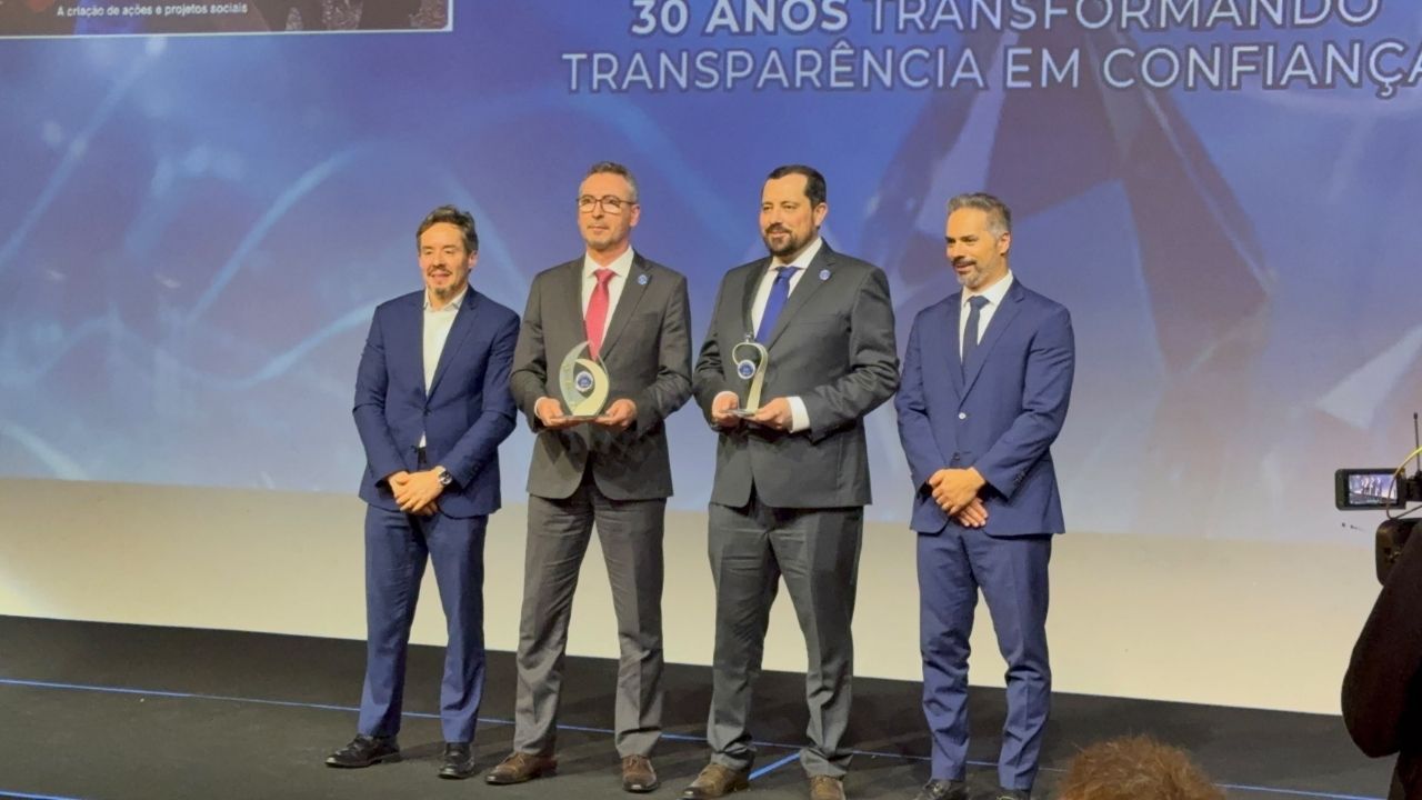 Quatro homens de terno estão de pé em um palco segurando troféus, em frente a um telão com a frase "30 anos transformando transparência em confiança"