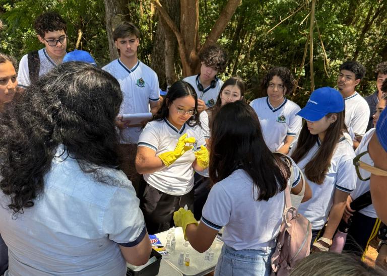alunos estão num espaço aberto proximo ao rio e estão analisando a qualidade da agua com kit 