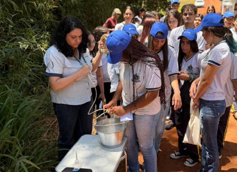 alunos estão num espaço aberto proximo ao rio e estão analisando a qualidade da agua com kit 
