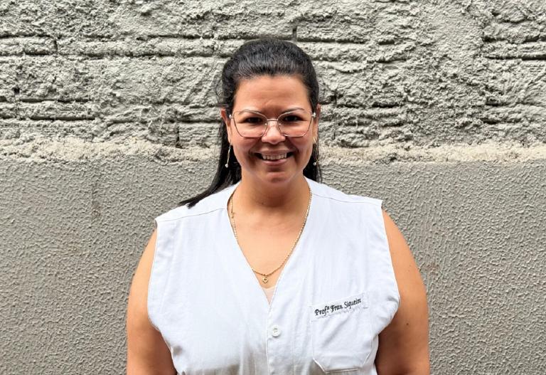 professora posa para foto com uniforme da escola e sorriso no rosto