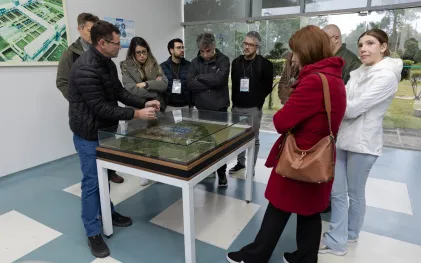 Grupo de visitantes observa uma maquete física detalhada de uma estação de tratamento de água sob proteção de vidro, enquanto um técnico da Sanepar faz explicações apontando para a estrutura