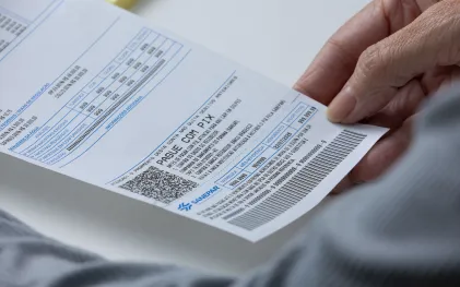 Mulher segurando uma fatura de uma conta de água, com um QR code para pagamentos via Pix em evidência