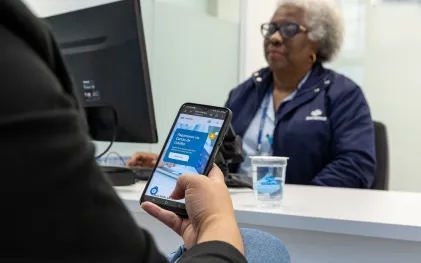 clientes está no atendimento da sanepar e está usando o celular. uma mulher negra e de cabelos brancos é a atendente