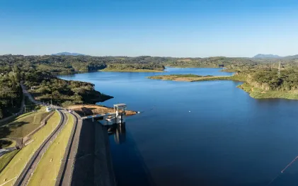 Vista panorâmica da Barragem do Miringuava com amplo reservatório de água cercado por vegetação e morros ao fundo sob céu limpo