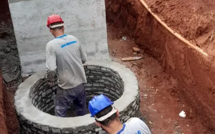 dois homens vestindo roupa cinza e capacete fazem obra civil com tijolos e cimento
