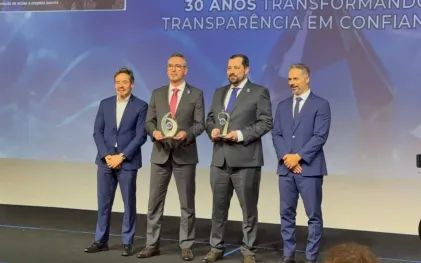 Quatro homens de terno estão de pé em um palco segurando troféus, em frente a um telão com a frase "30 anos transformando transparência em confiança"