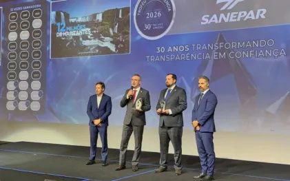 Quatro homens em um palco, sendo que um deles fala ao microfone segurando um troféu, com um telão ao fundo exibindo a marca Sanepar, o selo do Troféu Transparência 2026 e a frase "30 anos transformando transparência em confiança".