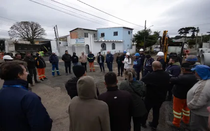 Vista ampliada de uma reunião técnica ao ar livre em uma rua residencial, onde trabalhadores e representantes da Sanepar e da prefeitura formam uma roda para acompanhar as orientações sobre a obra