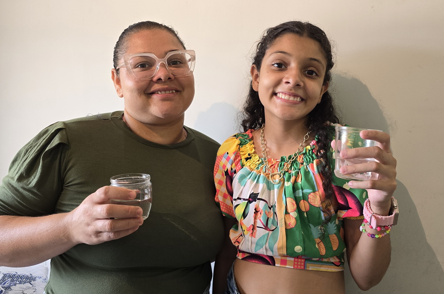 mãe e filha sorriem com copo de água na mão