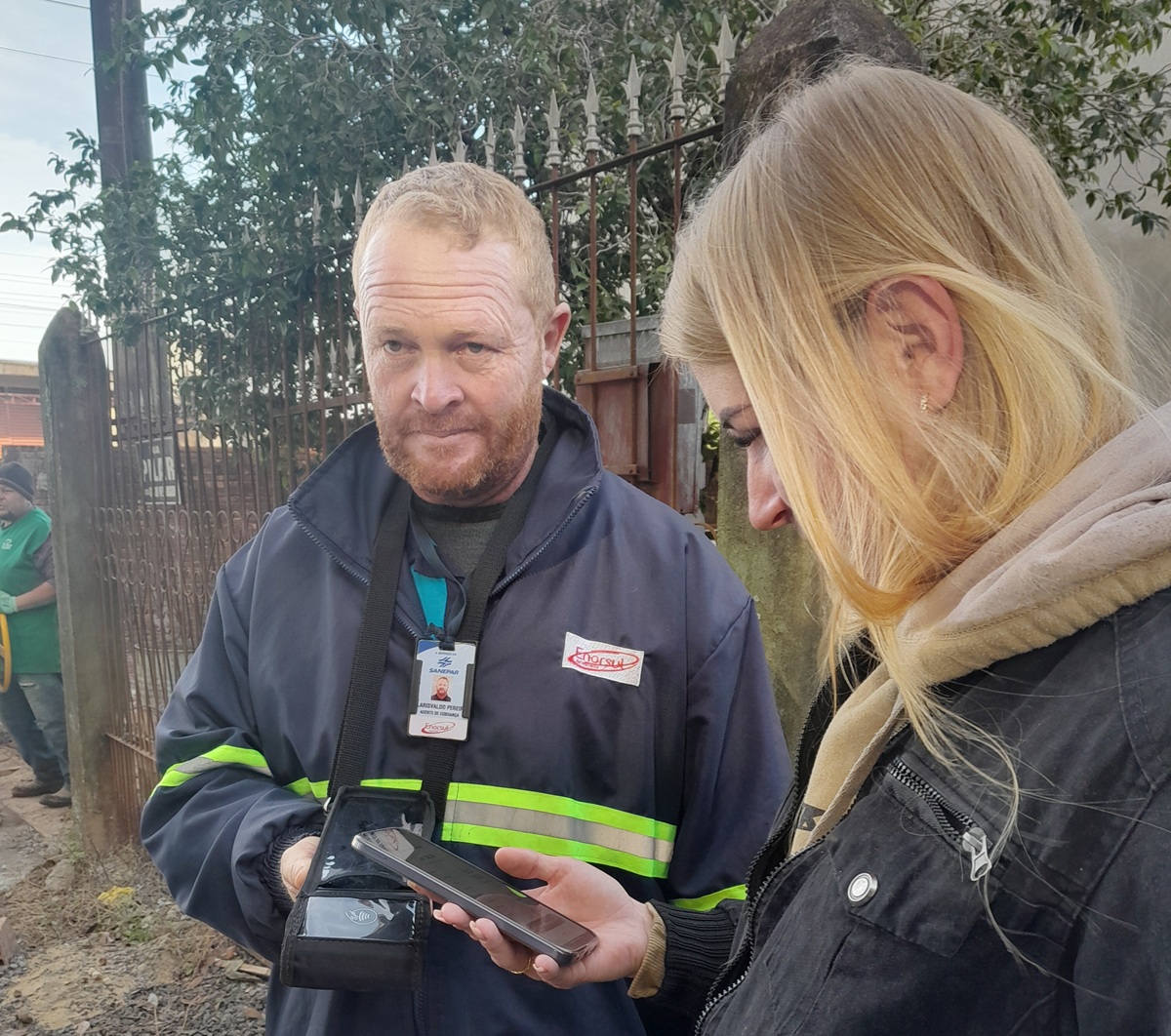 mostra um homem e uma mulher olhando para baixo, em direção a um smartphone que a mulher está segurando, indicando a possibilidade de pagamento de fatura da sanepar.