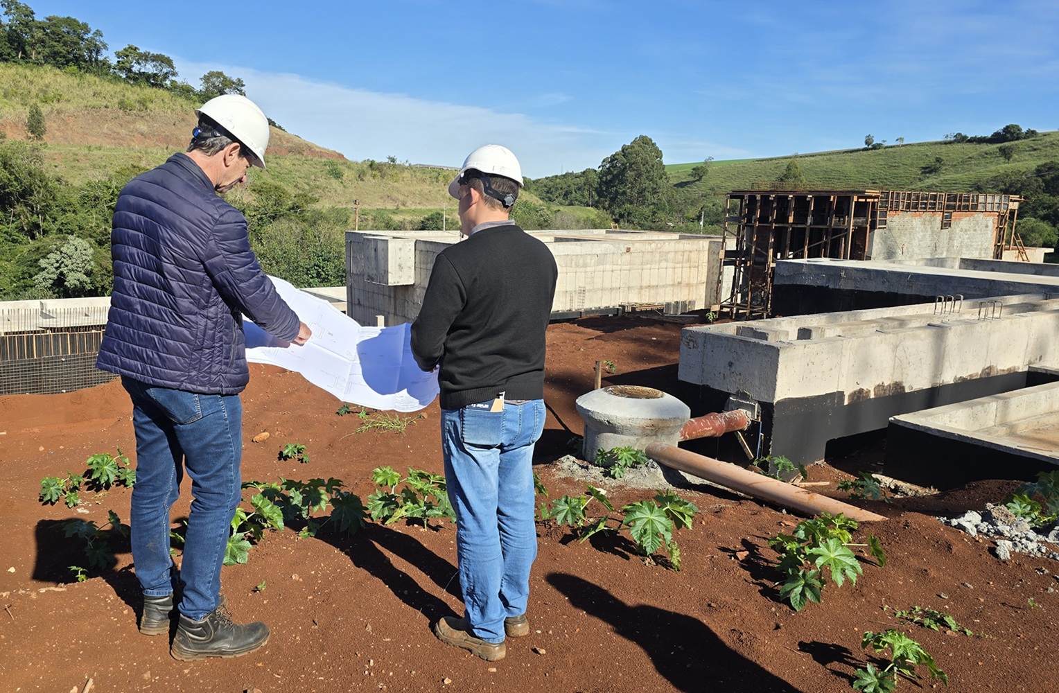 engenheiros com projeto da obra diante de estruturas de concreto em obra de estação de esgoto