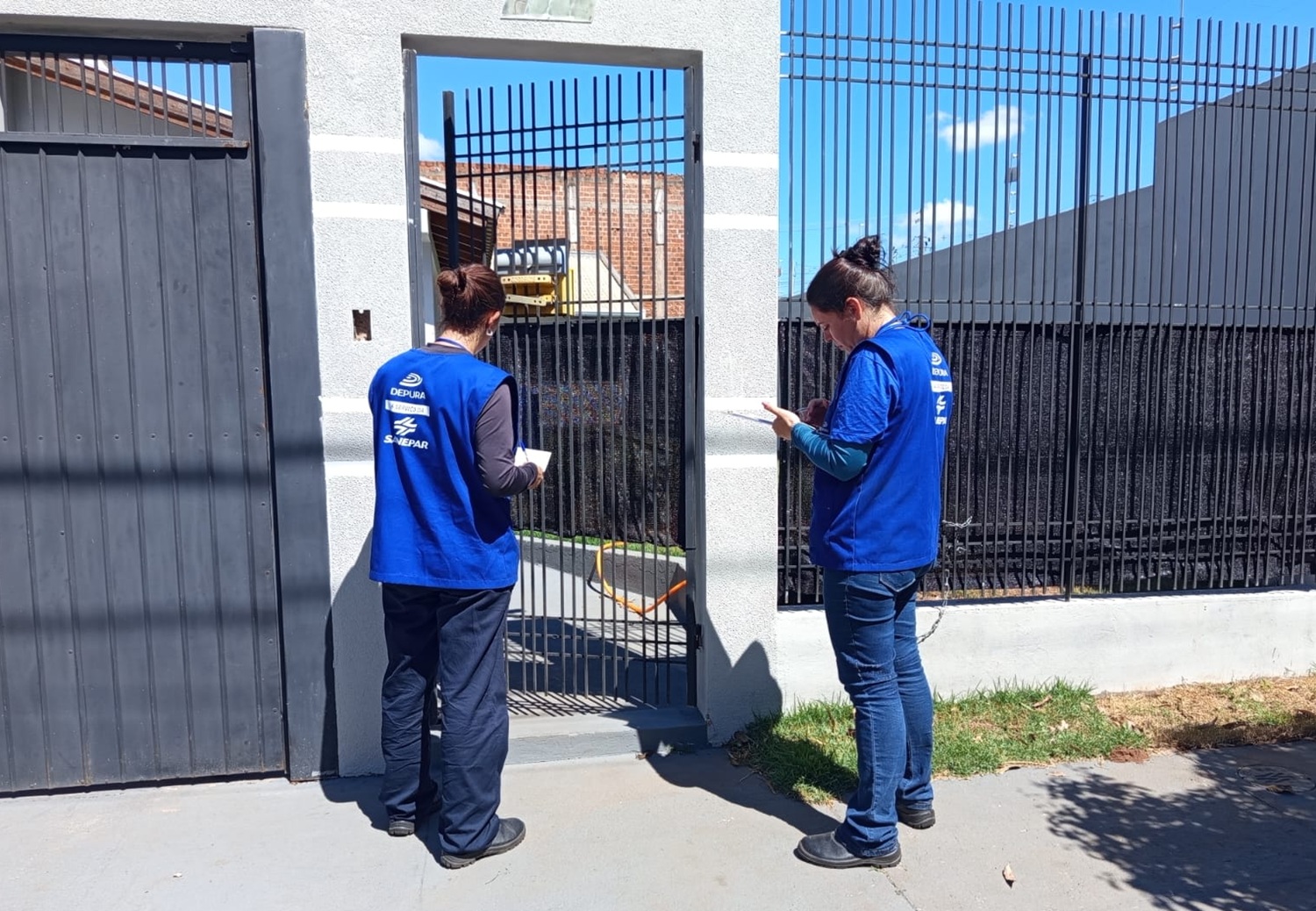 técnicos com uniformes da cor azul abordam clientes no portão de suas casas
