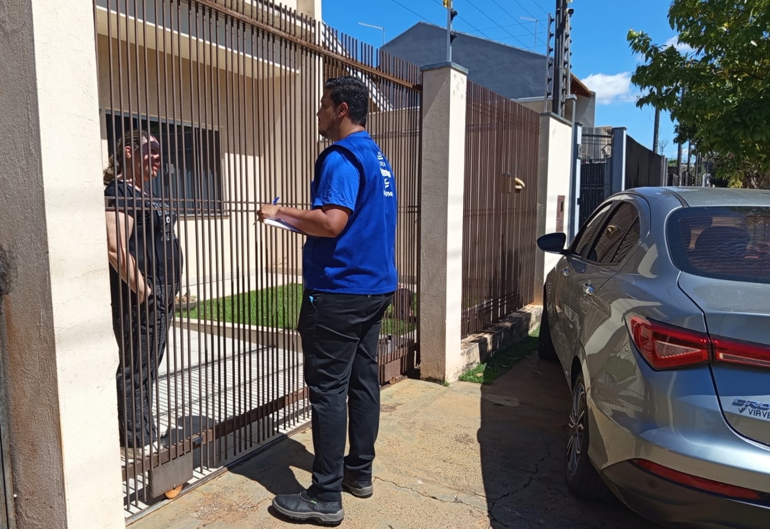 técnicos com uniformes da cor azul abordam clientes no portão de suas casas