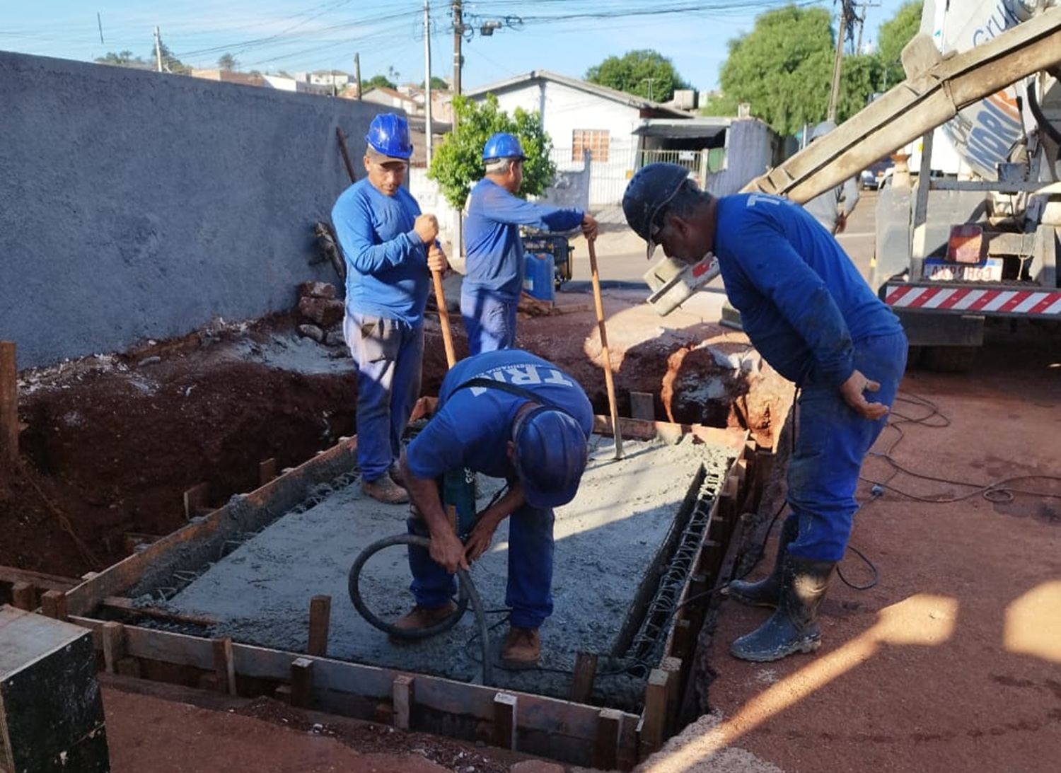 trabalhadores devidamente uniformizados e protegidos, com capacetes, trabalham na instalação de equipamentos, num caixa de concreto no chão