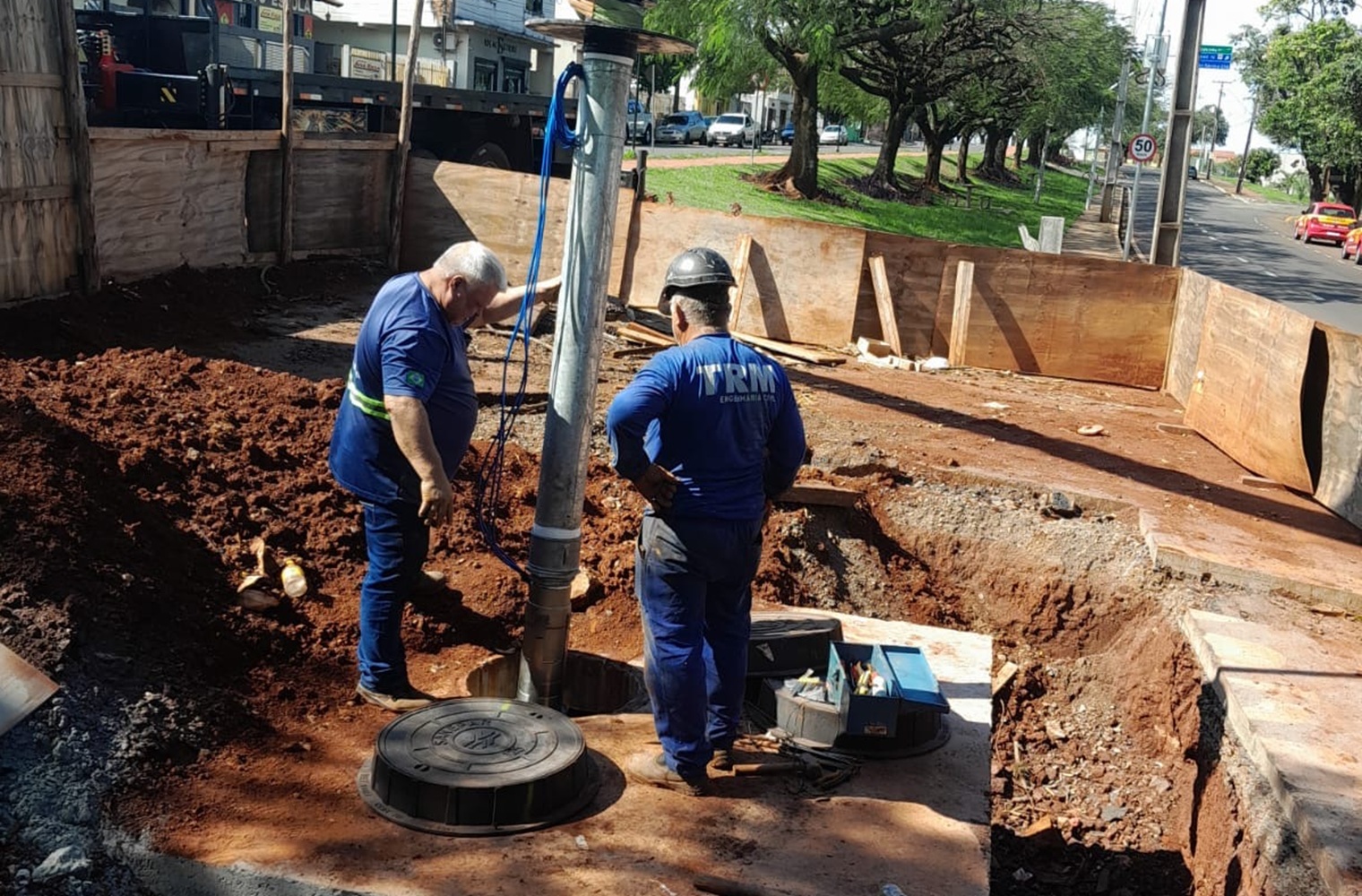 trabalhadores devidamente uniformizados e protegidos, com capacetes, trabalham na instalação de equipamentos, num caixa de concreto no chão