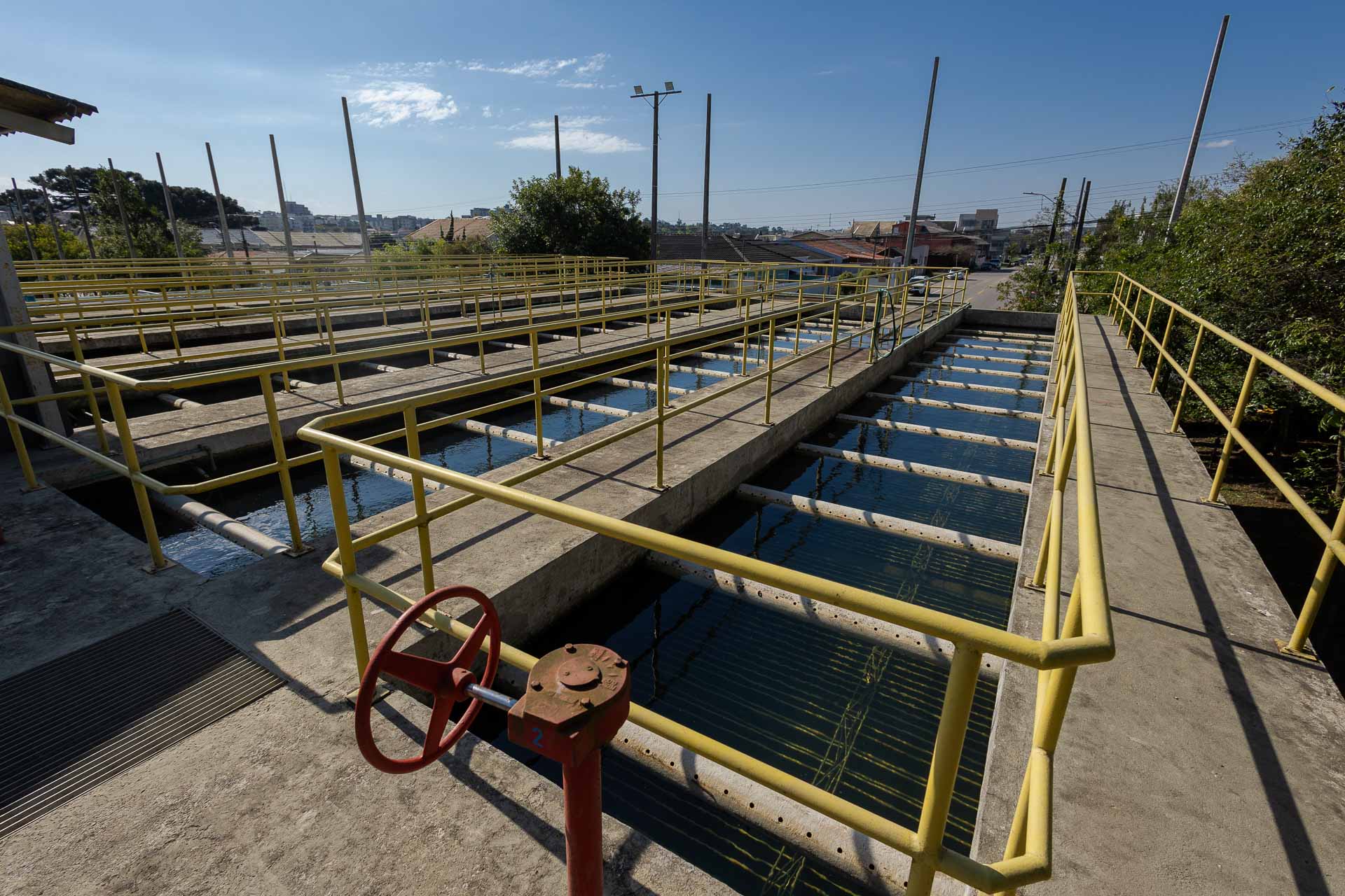 Vista em primeiro plano dos tanques de filtragem da estação de tratamento de água, com estrutura em concreto, guarda-corpos amarelos e um registro hidráulico em destaque.