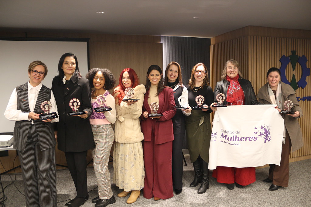 Mulheres enfileiradas lado a lado exibem a bandeira do coletivo de mulheres do Senge-PR.