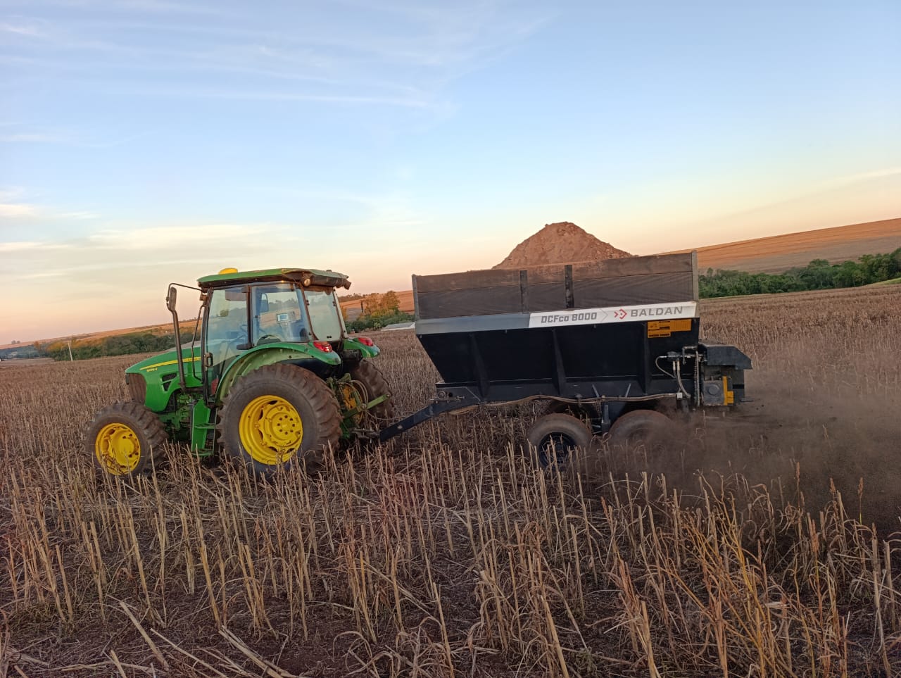 Trator agrícola realiza a aplicação de insumos e correção do solo em plantação sob a luz do pôr do sol