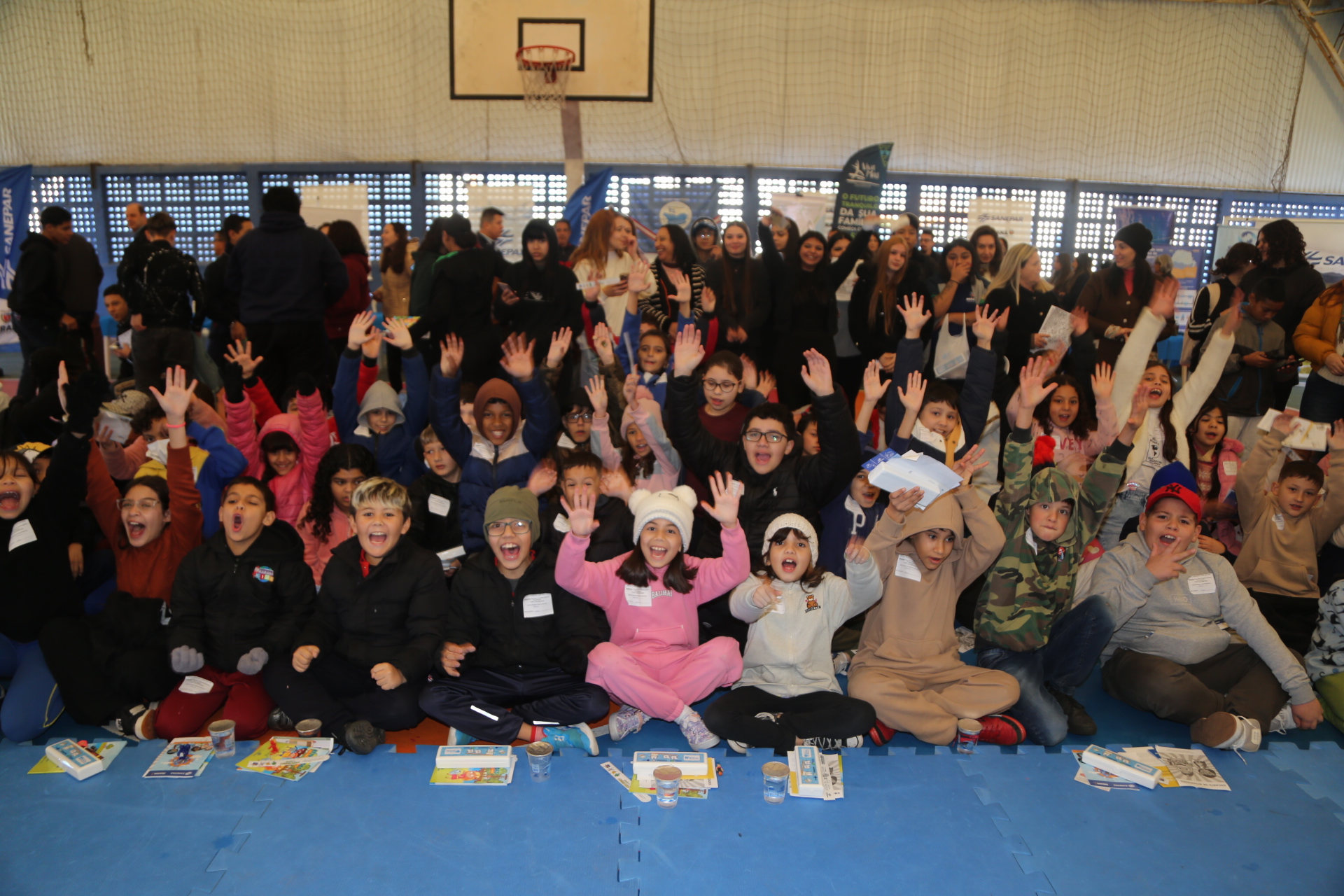 Crianças alinhadas com as mãos para o alto durante um evento da Sanepar.