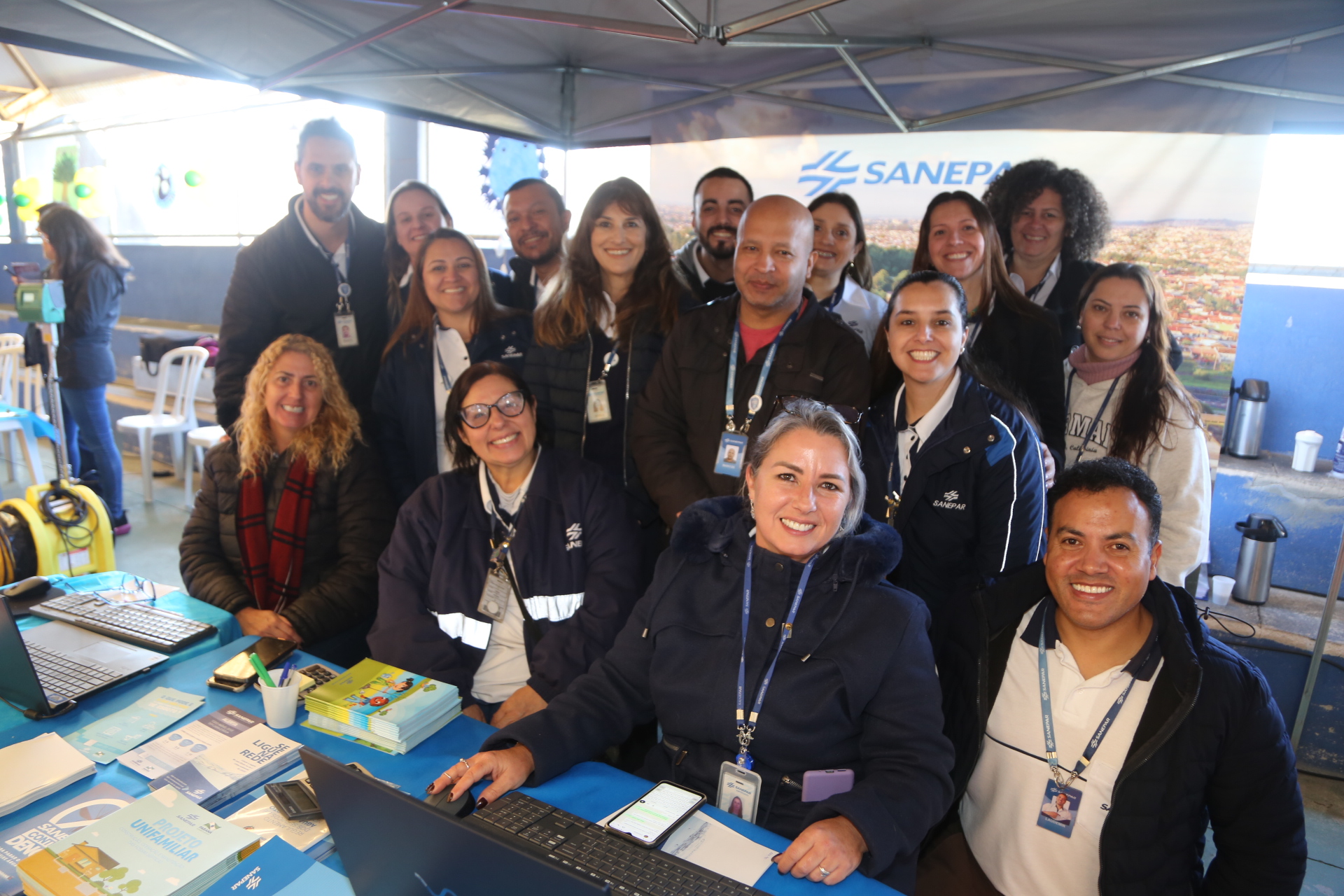 Equipe da Sanepar posa para foto. Parte dos empregados está sentada e outra parte alinhada ao fundo. Todos, homens e mulheres, estão uniformizados.