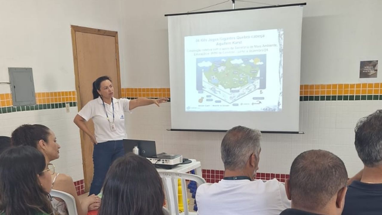 Palestrante apontando para projeção em slide sobre jogos de quebra-cabeça do Aquífero Karst durante apresentação de conscientização ambiental.