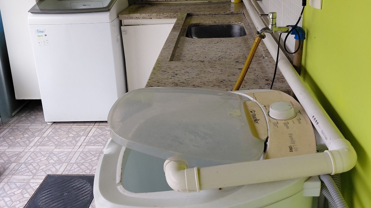 Tanquinho de lavar roupas com tubulação de PVC adaptada para direcionar o descarte de água, instalado em lavanderia residencial.