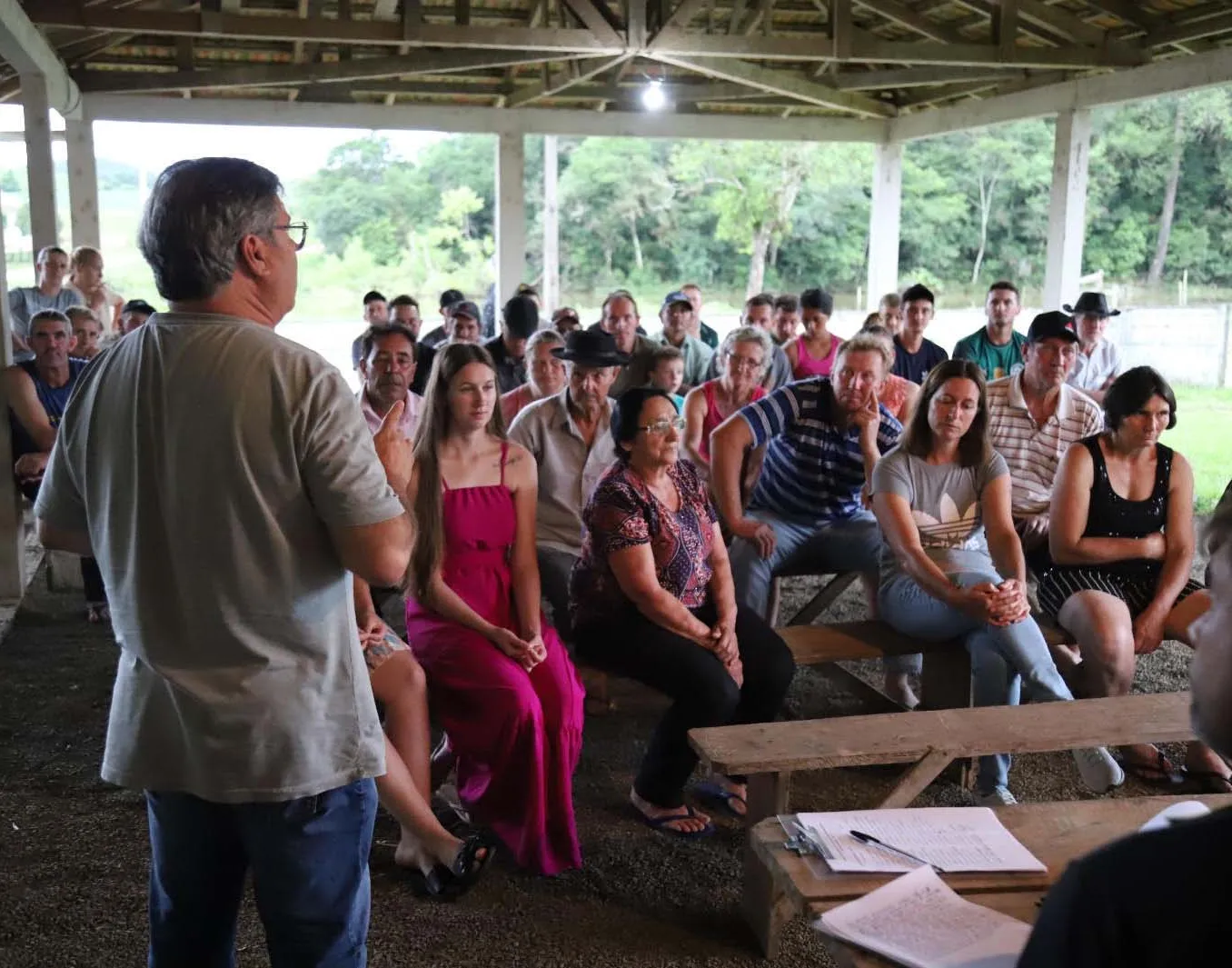 Comunidade de pessoas reunidas em um pequeno galpão, ouvindo uma palestra.