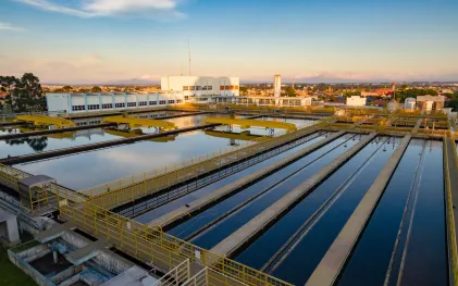 Vista aérea dos tanques de decantação e filtragem da ETA Iguaçu sob a luz do pôr do sol, com prédio operacional ao fundo.