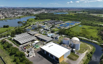 Vista aérea panorâmica da Estação de Tratamento de Esgoto Belém, exibindo os tanques circulares de decantação, lagoas de tratamento e os grandes biodigestores cilíndricos brancos ao lado do rio.