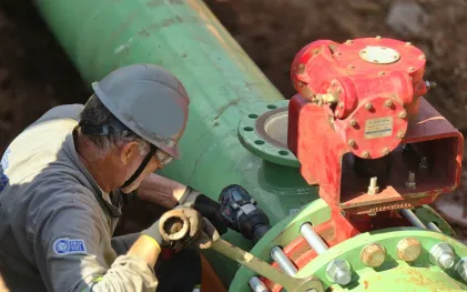 operário, devidamente equipado e com ferramentas, aperta parafusos em  uma conexão de tubulação 