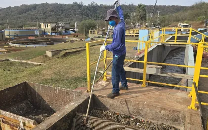 trabalhador devidamente equipado com máscara, retira resíduos sólidos de gradeamento na entrada da estação de tratamento de esgoto
