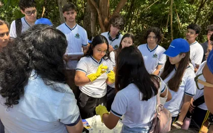 alunos estão num espaço aberto proximo ao rio e estão analisando a qualidade da agua com kit 