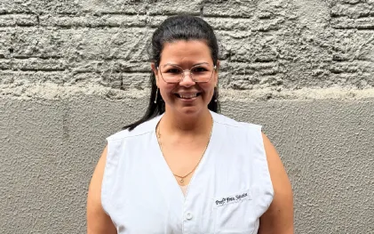 professora posa para foto com uniforme da escola e sorriso no rosto
