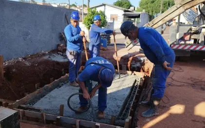 trabalhadores devidamente uniformizados e protegidos, com capacetes, trabalham na instalação de equipamentos, num caixa de concreto no chão