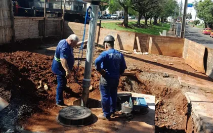 trabalhadores devidamente uniformizados e protegidos, com capacetes, trabalham na instalação de equipamentos, num caixa de concreto no chão