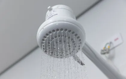 Chuveiro elétrico branco em funcionamento, projetando filetes finos de água caindo