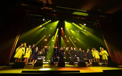 grupo vocal em apresentação musical num palco bastante iluminado