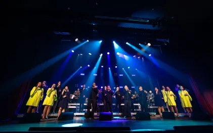 grupo vocal em apresentação musical num palco bastante iluminado