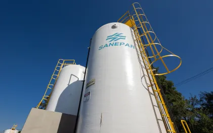 Dois grandes reservatórios cilíndricos brancos com a logomarca da Sanepar em azul, com escadas de acesso amarelas contra um céu azul limpo.