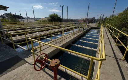 Vista em primeiro plano dos tanques de filtragem da estação de tratamento de água, com estrutura em concreto, guarda-corpos amarelos e um registro hidráulico em destaque.