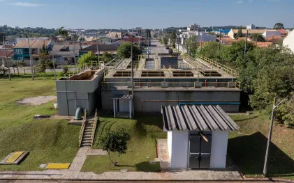 Vista aérea do complexo da Estação de Tratamento de Água (ETA) em Araucária, destacando os tanques de tratamento em concreto e guarda-corpos amarelos, cercados por área verde e casas do bairro ao fundo