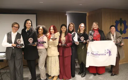 Mulheres enfileiradas lado a lado exibem a bandeira do coletivo de mulheres do Senge-PR.