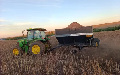 Trator agrícola realiza a aplicação de insumos e correção do solo em plantação sob a luz do pôr do sol