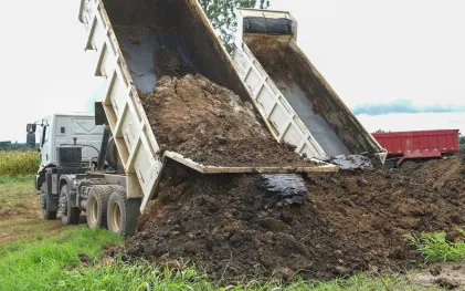 Dois caminhões basculantes da Sanepar descarregando lodo de esgoto higienizado em um monte ao lado da lavoura
