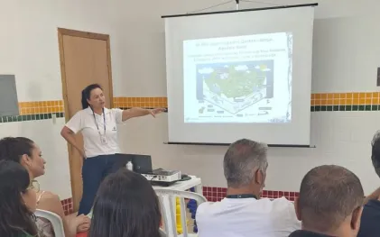 Palestrante apontando para projeção em slide sobre jogos de quebra-cabeça do Aquífero Karst durante apresentação de conscientização ambiental.