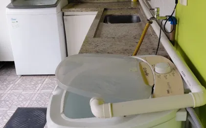Tanquinho de lavar roupas com tubulação de PVC adaptada para direcionar o descarte de água, instalado em lavanderia residencial.