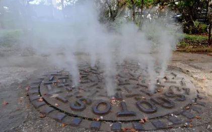 Plumas de fumaça branca saindo através dos orifícios de uma tampa circular de bueiro de esgoto na calçada