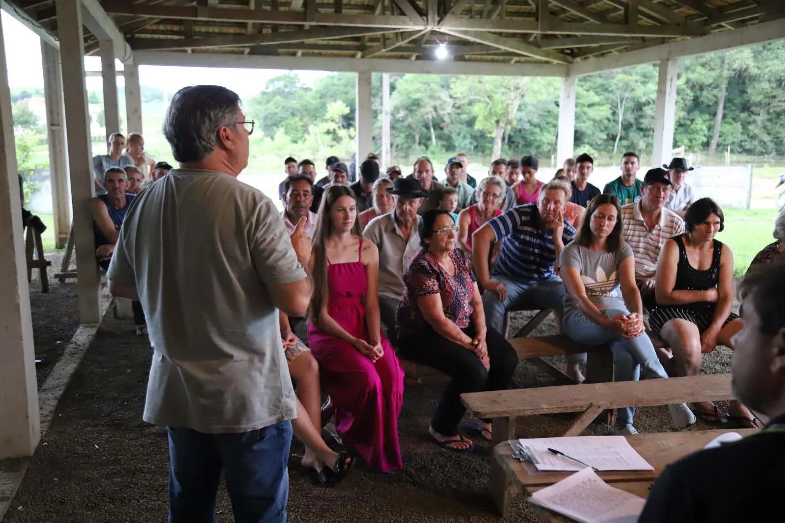 Comunidade de pessoas reunidas em um pequeno galpão, ouvindo uma palestra.